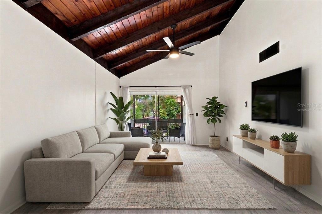 A living room with a vaulted wood-beam ceiling, sectional sofa, and a large television — 10415 CARROLLBROOK CIRCLE UNIT 207, TAMPA, FL
