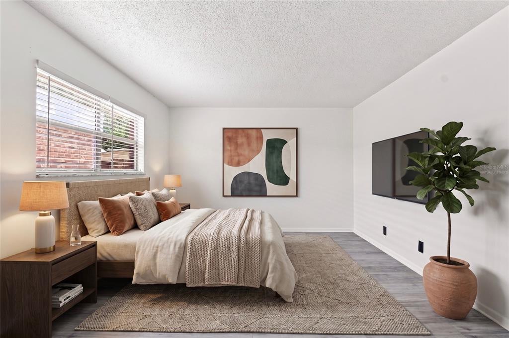 A bedroom features a bed with neutral bedding, a wall-mounted television, and a potted plant — 10415 CARROLLBROOK CIRCLE UNIT 207, TAMPA, FL
