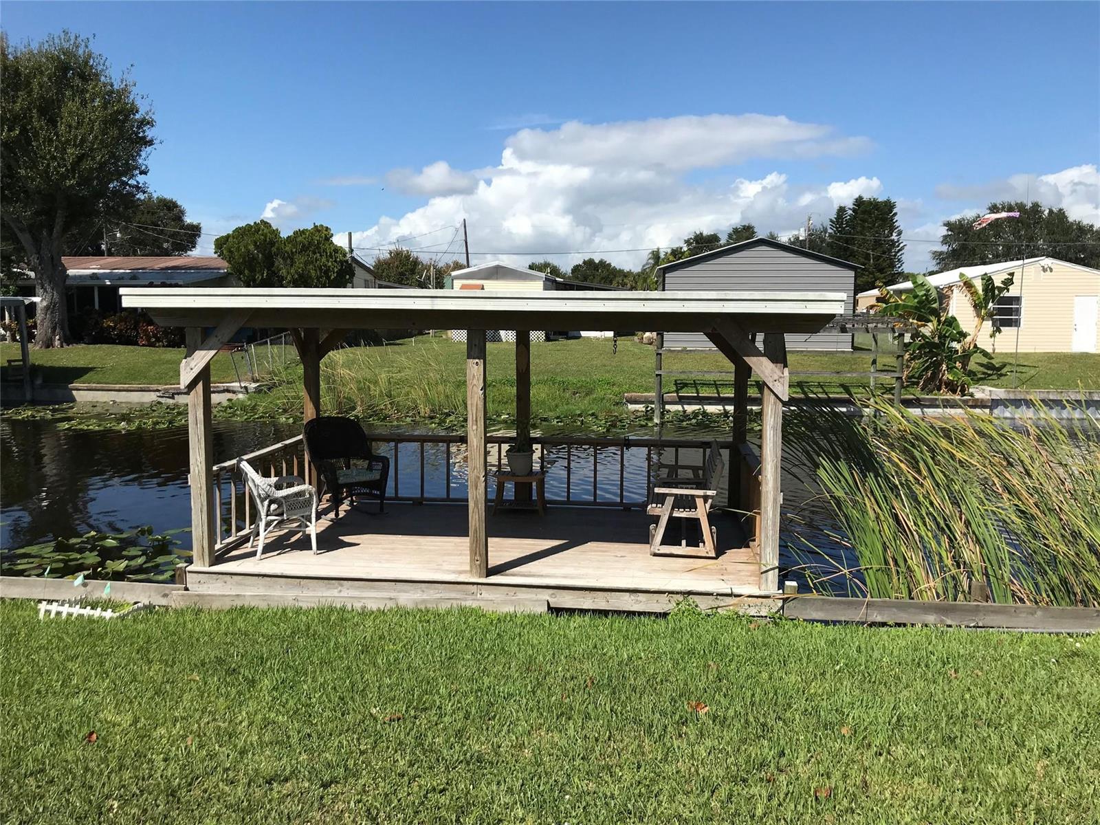 A wooden deck with a roof sits over a canal, featuring chairs and a railing — 1112 21st Street, Okeechobee FL 34974, OKEECHOBEE, FL