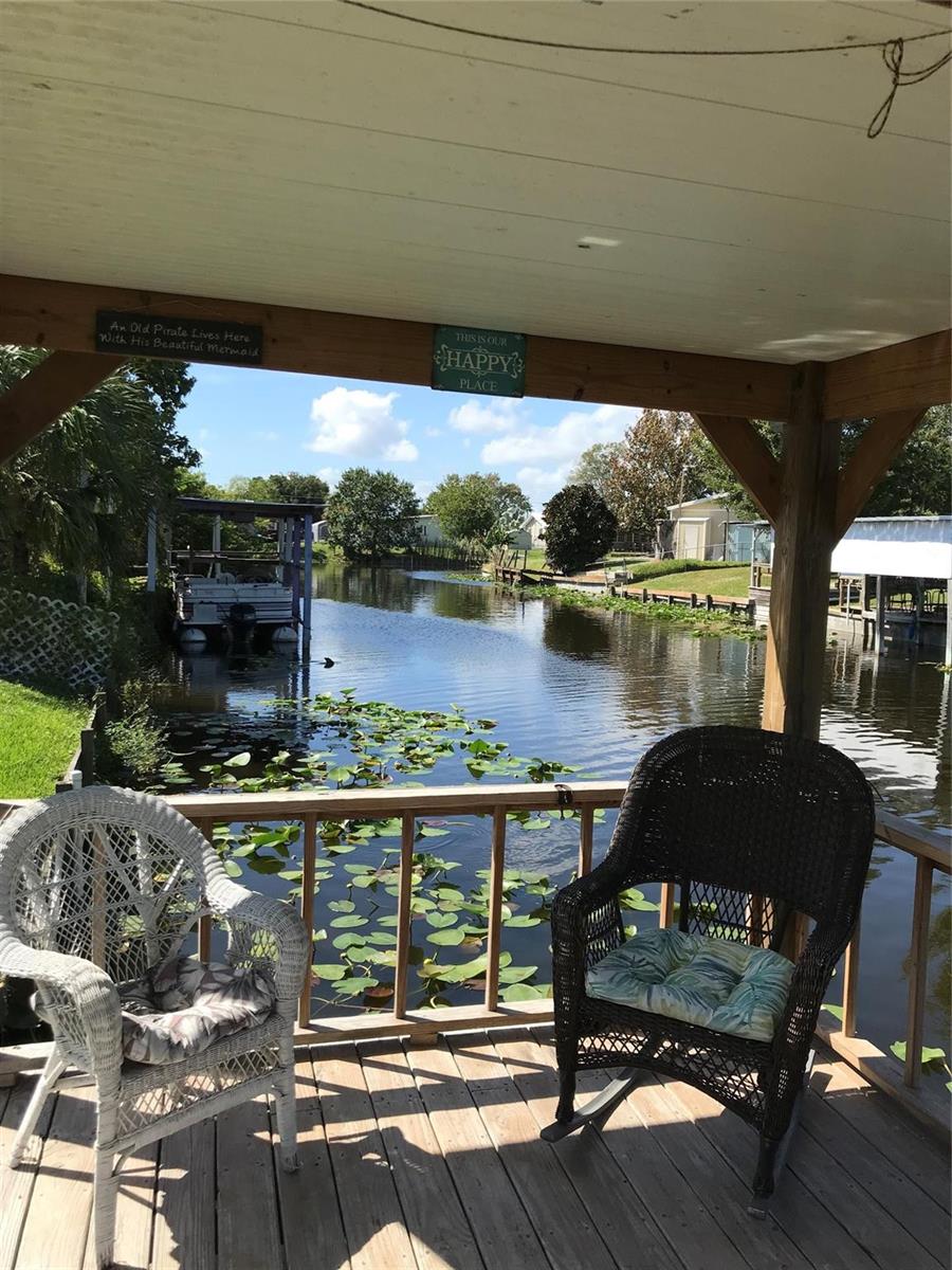 A covered wooden deck overlooks a canal with two wicker chairs and decorative signs — 1112 21st Street, Okeechobee FL 34974, OKEECHOBEE, FL