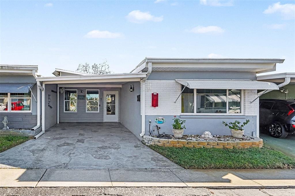 A single-story house features a gray exterior, a covered carport, and a small front garden — 250 ROSERY ROAD NW UNIT 219, LARGO, FL