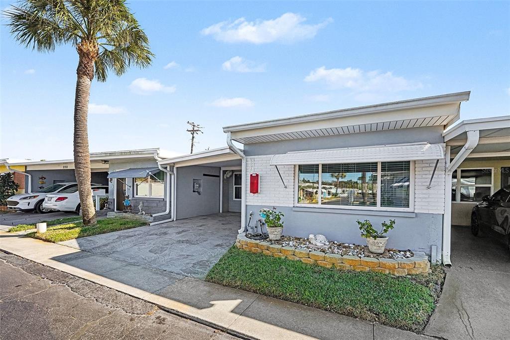 A single-story house with a gray exterior, a carport, and a small stone-walled garden — 250 ROSERY ROAD NW UNIT 219, LARGO, FL