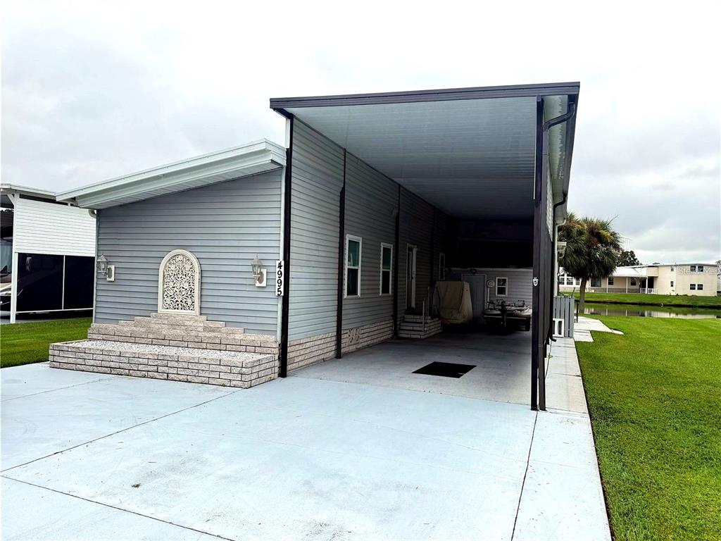 A gray manufactured home features a large attached carport and a decorative stone-accented front entrance — 4995 MOUNT OLIVE SHORES DRIVE, POLK CITY, FL