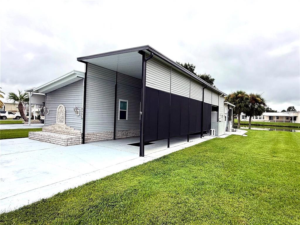 A gray manufactured home features a large attached carport with black privacy screening — 4995 MOUNT OLIVE SHORES DRIVE, POLK CITY, FL