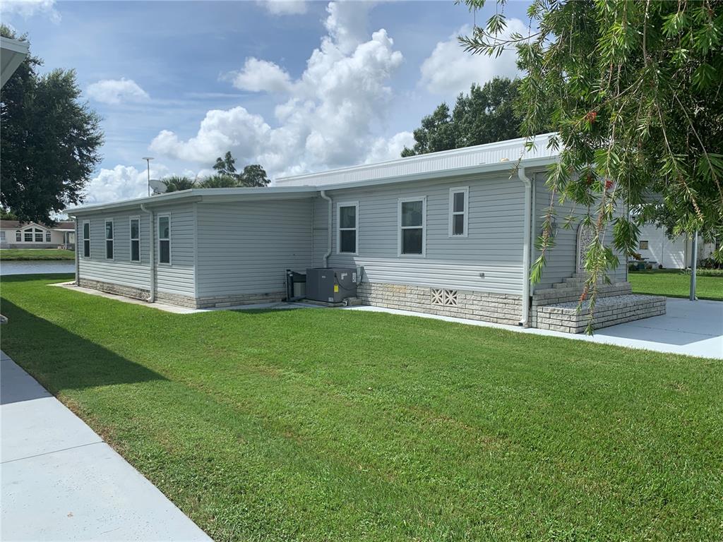 A light gray manufactured home with a brick-patterned foundation sits on a green lawn — 4995 MOUNT OLIVE SHORES DRIVE, POLK CITY, FL