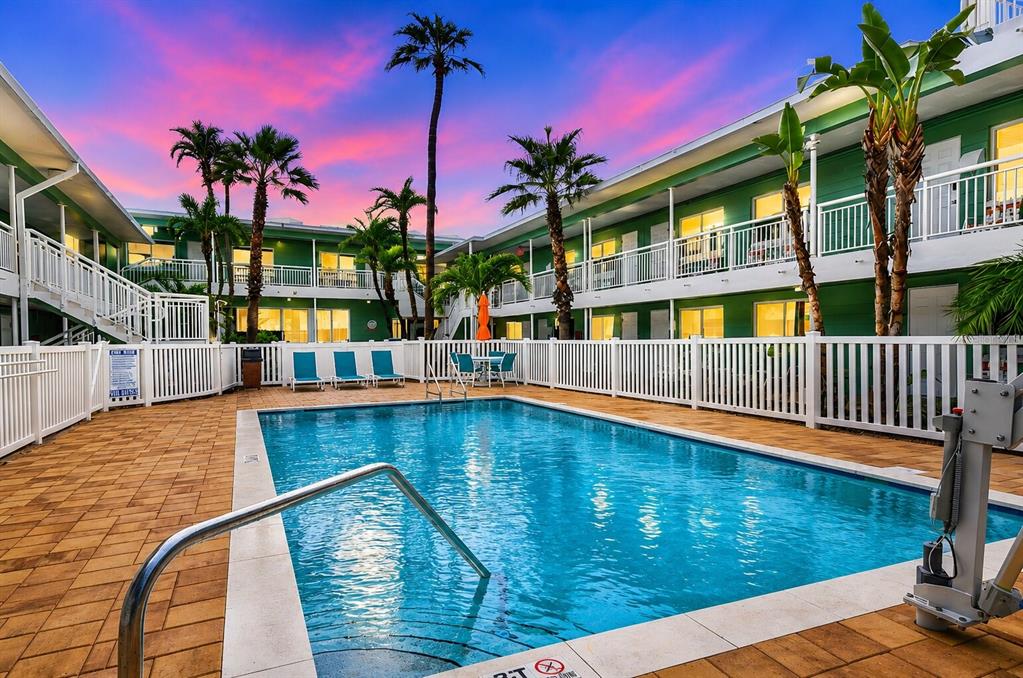 A swimming pool sits in the courtyard of a two-story green motel at sunset — 11730 GULF BOULEVARD UNIT 32, ST PETERSBURG, FL