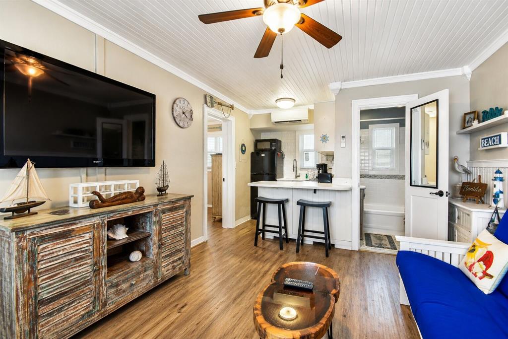 A living room features wood-look flooring, a ceiling fan, a television, and a small kitchen — 11730 GULF BOULEVARD UNIT 32, ST PETERSBURG, FL