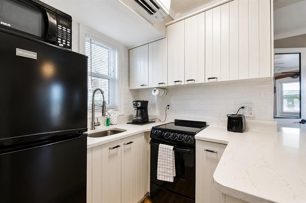 A small kitchen features white cabinetry, black appliances, a subway tile backsplash, and quartz countertops — 11730 GULF BOULEVARD UNIT 32, ST PETERSBURG, FL