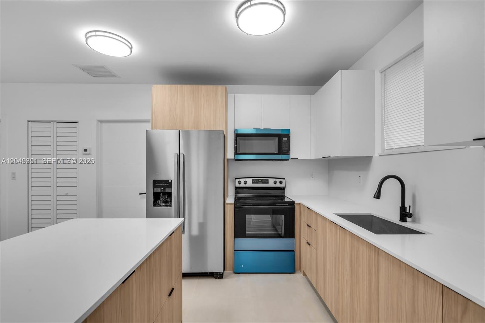 A modern kitchen features light wood cabinetry, white countertops, stainless steel appliances, and a blue stove — 6500 NW 21st Ave # 6500, Miami FL 33147, MIAMI, FL