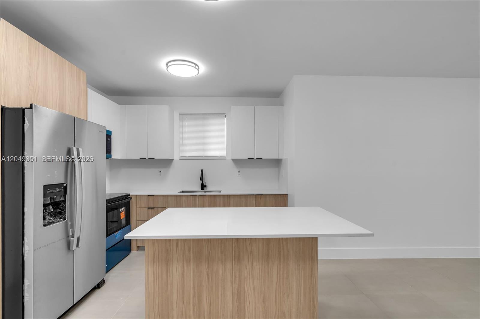 A modern kitchen features white upper cabinets, light wood lower cabinets, and a central island — 6500 NW 21st Ave # 6500, Miami FL 33147, MIAMI, FL