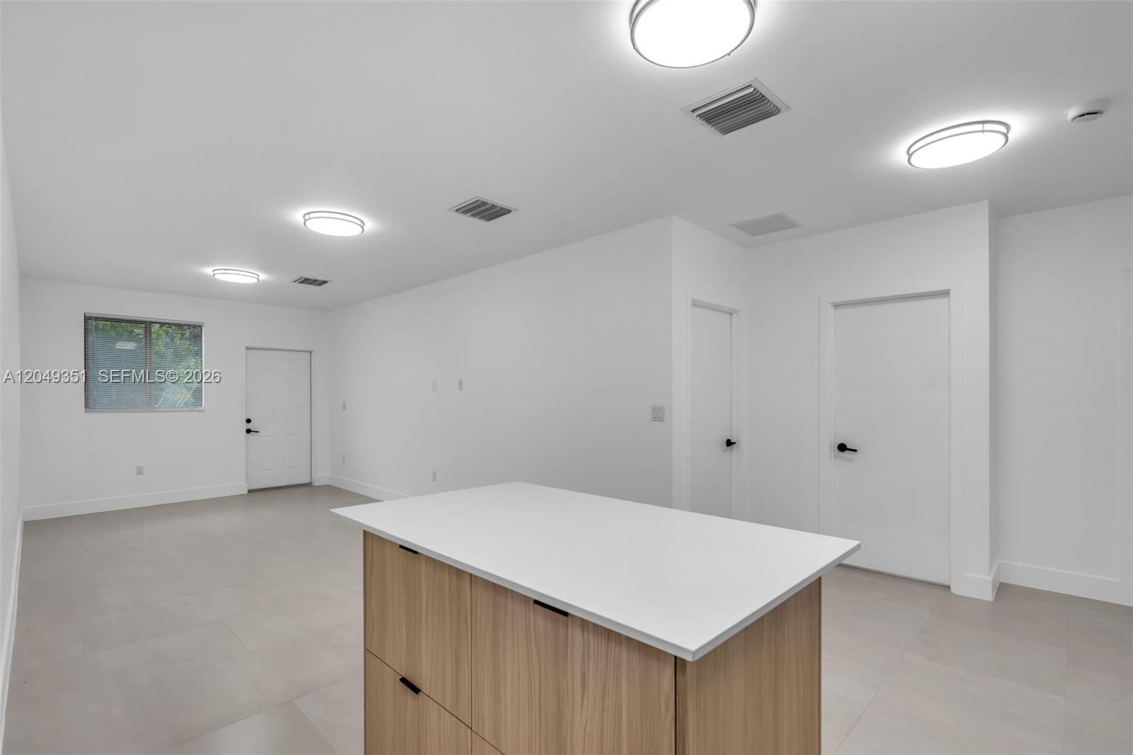 A minimalist room features a kitchen island, white walls, recessed lighting, and two closed doors — 6500 NW 21st Ave # 6500, Miami FL 33147, MIAMI, FL