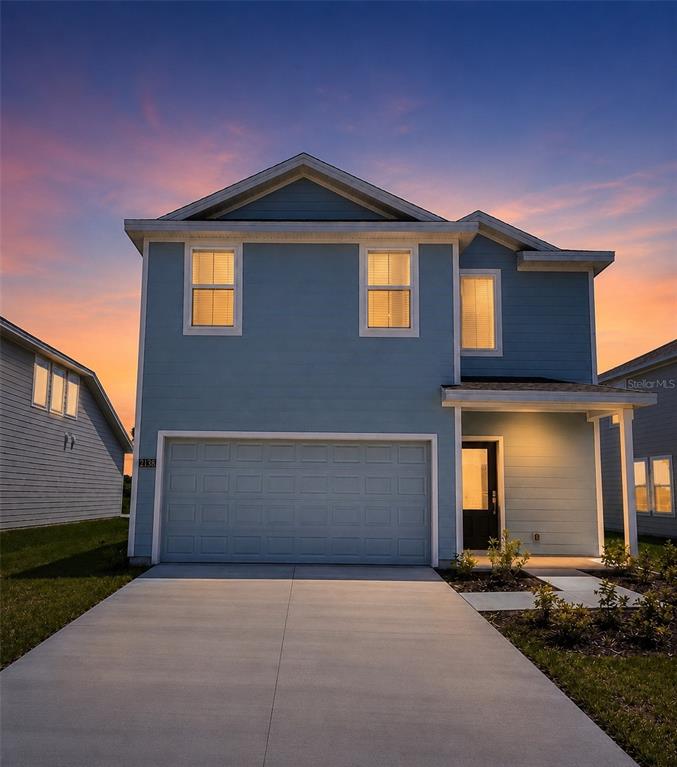 A two-story blue house with a garage and a concrete driveway at sunset — 3055 GRANITE RIDGE AVENUE, MINNEOLA, FL