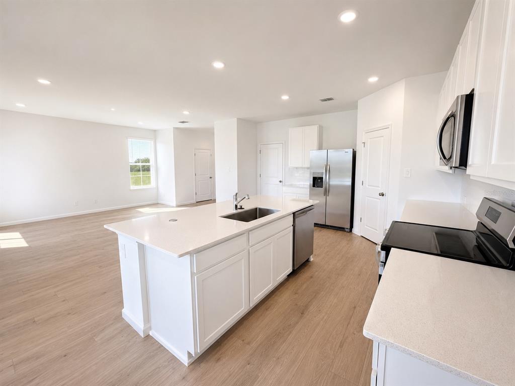 A modern kitchen with white cabinets, quartz countertops, and a central island overlooks an open living area — 3055 GRANITE RIDGE AVENUE, MINNEOLA, FL
