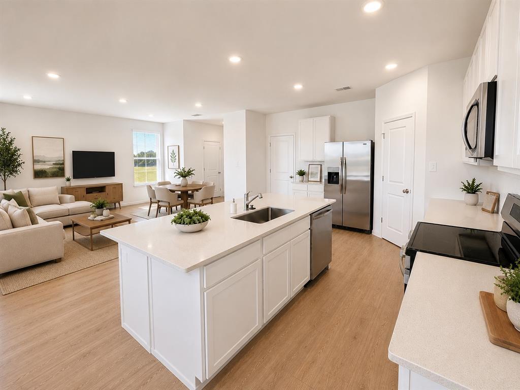 A modern open-concept kitchen and living area features white cabinetry, a central island, and wood-look flooring — 3055 GRANITE RIDGE AVENUE, MINNEOLA, FL