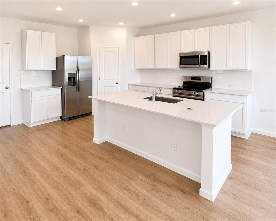 A modern kitchen features white cabinets, stainless steel appliances, a center island, and wood-look flooring — 3055 GRANITE RIDGE AVENUE, MINNEOLA, FL