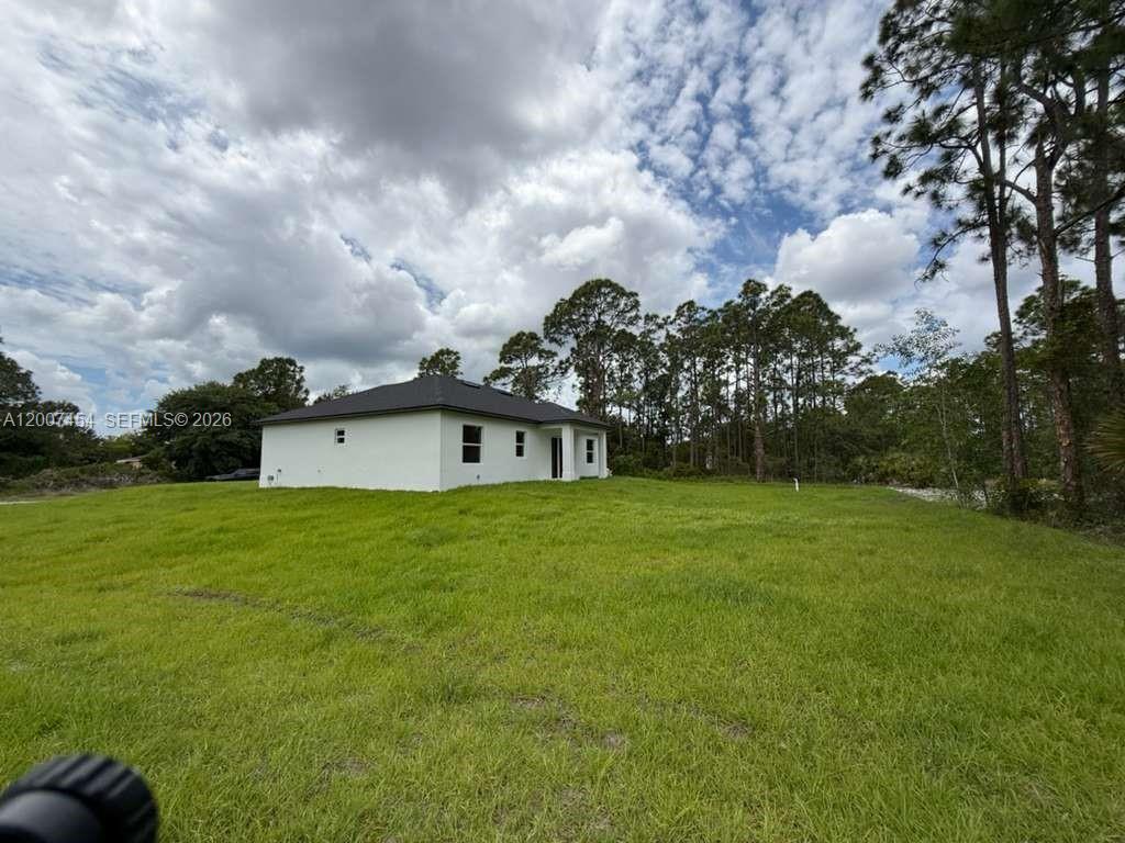 A white single-story house sits on a large, grassy lot surrounded by pine trees — 723 EPPS BROWN ST E # 723, Lehigh Acres FL 33974, LEHIGH ACRES, FL