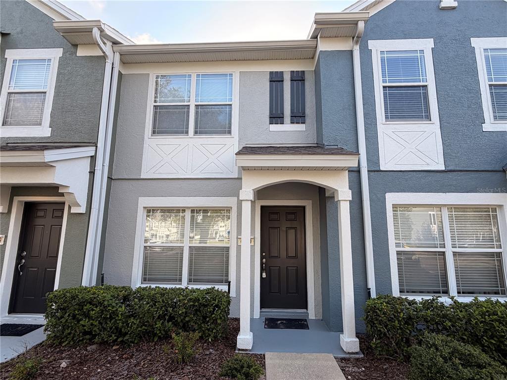 The exterior of a two-story townhouse features a covered entryway, dark doors, and light-colored siding — 4430 SW 49TH AVENUE, OCALA, FL