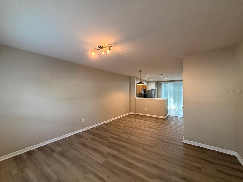 An open-concept living area features light-colored walls, wood-look flooring, and a view into the kitchen — 4430 SW 49TH AVENUE, OCALA, FL