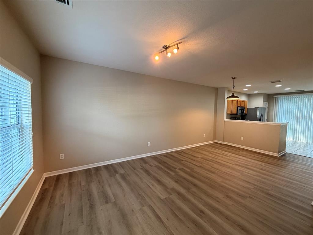 An empty living room with wood-look flooring, beige walls, and an adjacent open kitchen — 4430 SW 49TH AVENUE, OCALA, FL