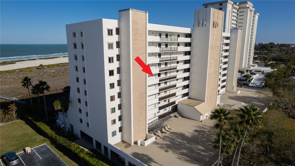 An aerial view of a multi-story beachfront condominium building with a red arrow pointing toward a balcony — 1250 GULF BOULEVARD UNIT 703, CLEARWATER BEACH, FL
