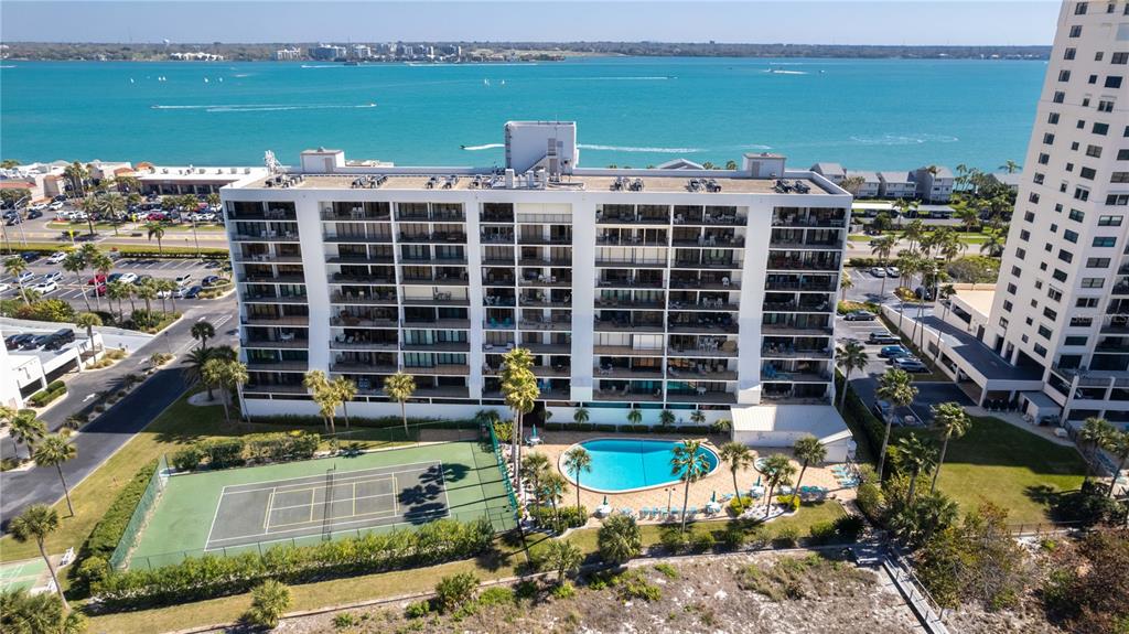 An aerial view shows a multi-story apartment building with a tennis court and swimming pool — 1250 GULF BOULEVARD UNIT 703, CLEARWATER BEACH, FL