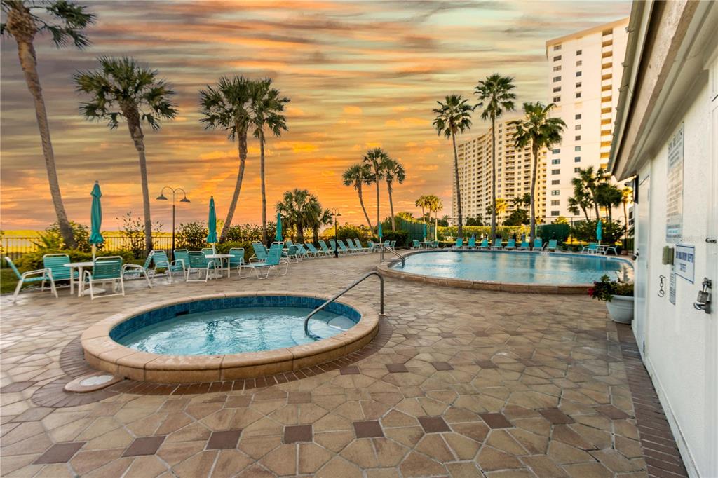 A pool deck features a circular hot tub, a swimming pool, lounge chairs, and palm trees — 1250 GULF BOULEVARD UNIT 703, CLEARWATER BEACH, FL