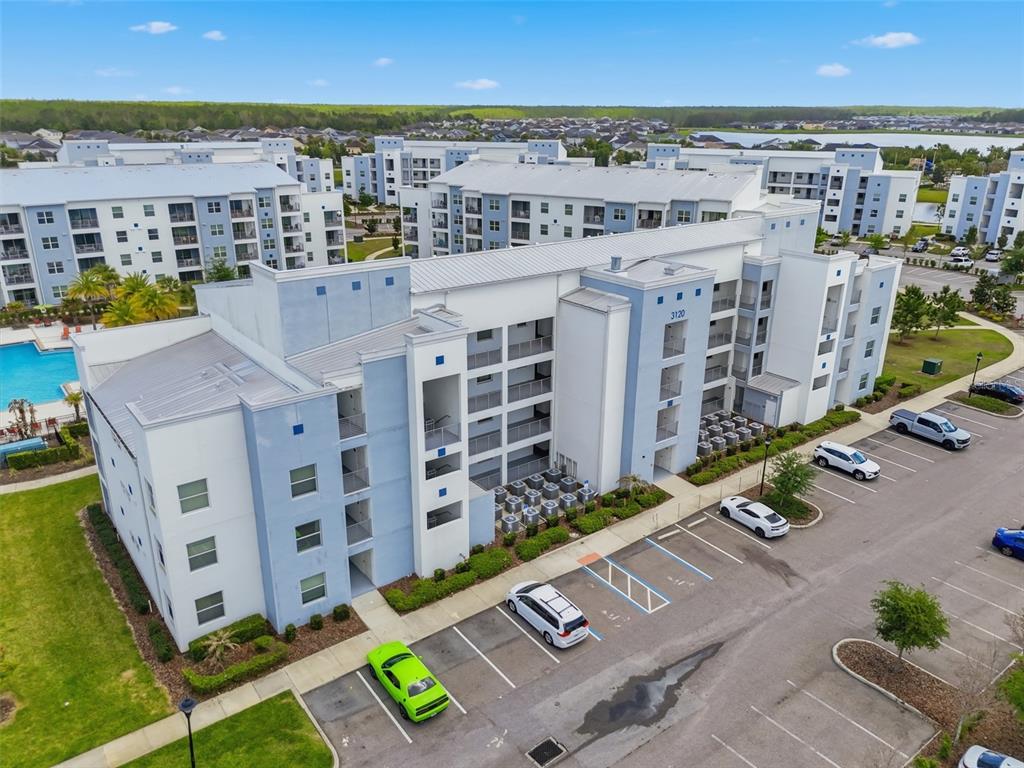 An aerial view shows a multi-story apartment building with a parking lot and swimming pool — 3120 PARADOX CIRCLE UNIT 302, KISSIMMEE, FL