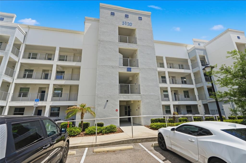 A multi-story apartment building exterior features white stucco walls, balconies with metal railings, and parking — 3120 PARADOX CIRCLE UNIT 302, KISSIMMEE, FL
