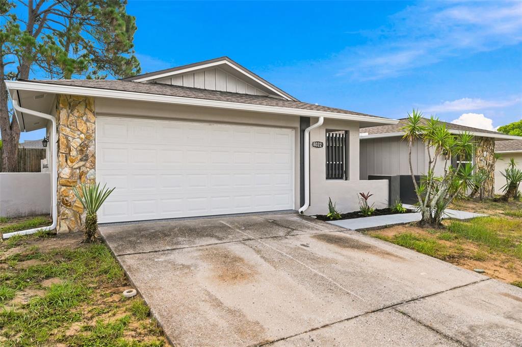 A single-story house features a white garage door, stone siding, and a concrete driveway — 8022 IDLEBRIAR LANE, PORT RICHEY, FL