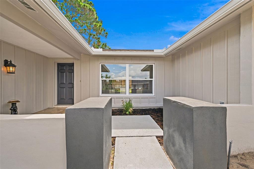 A concrete walkway leads to the front entrance of a house with light-colored siding — 8022 IDLEBRIAR LANE, PORT RICHEY, FL