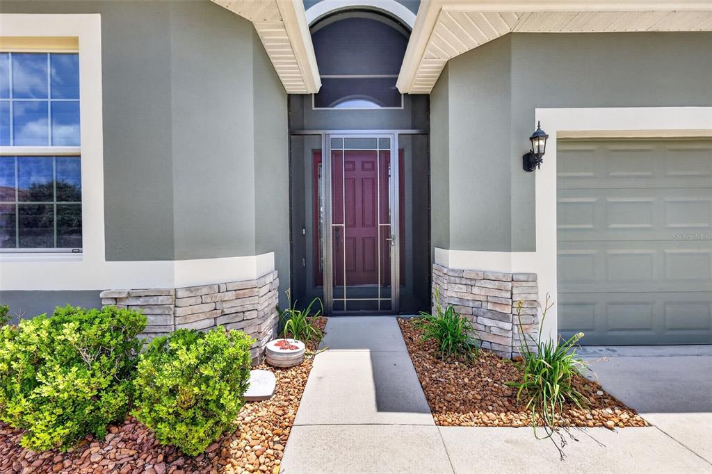 A front entryway with a red door, stone veneer accents, and a concrete walkway — 8716 BRIDGEPORT BAY CIRCLE, MOUNT DORA, FL