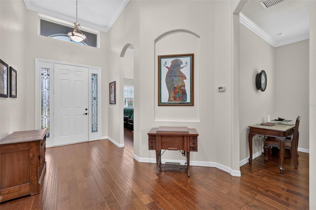 A bright foyer features hardwood floors, a white front door, and an arched wall niche — 8716 BRIDGEPORT BAY CIRCLE, MOUNT DORA, FL