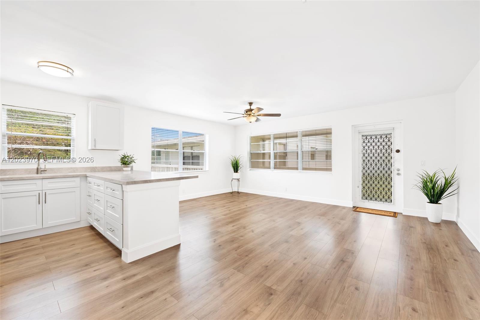 A bright, open-concept kitchen and living area features white cabinetry, wood-look flooring, and windows — 17 Lyndhurst # A, Deerfield Beach FL 33442, DEERFIELD BEACH, FL