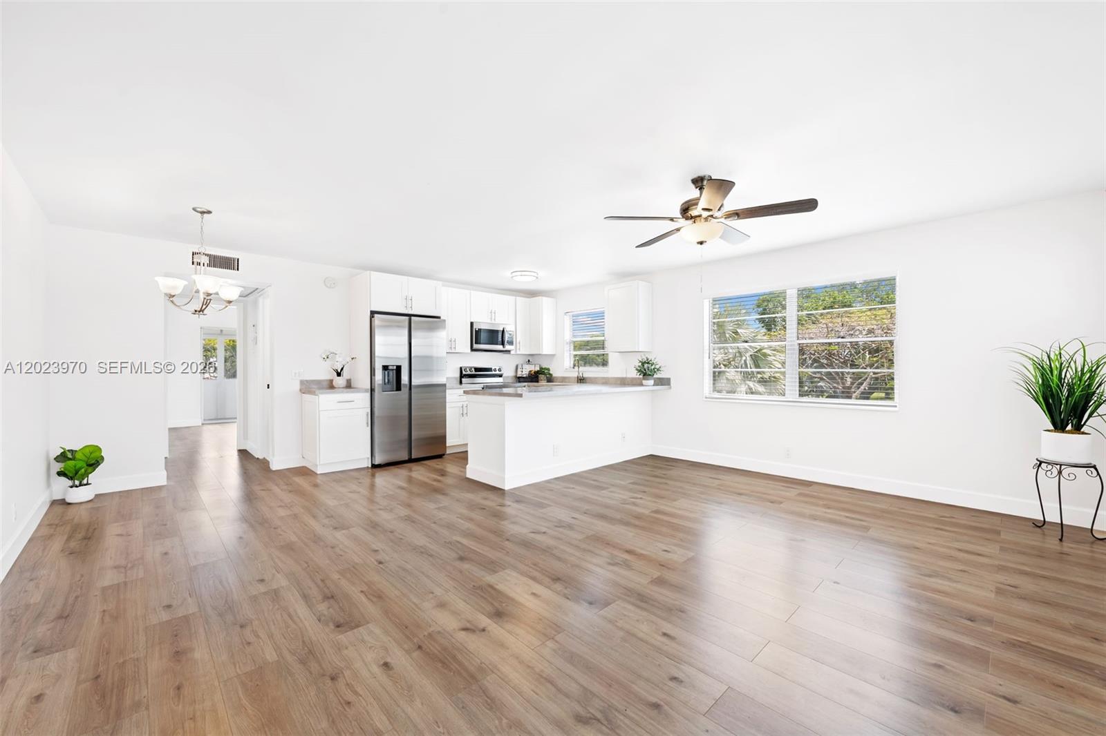 This open-concept kitchen and living area features white cabinetry, stainless steel appliances, and wood flooring — 17 Lyndhurst # A, Deerfield Beach FL 33442, DEERFIELD BEACH, FL