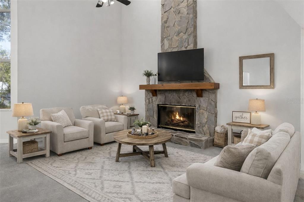 A living room features a stone fireplace, a television, and neutral-toned furniture on a rug — 5248 NEFF LAKE ROAD, BROOKSVILLE, FL