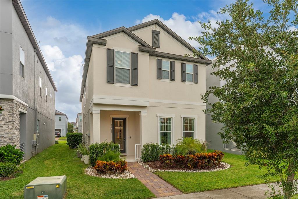 A two-story beige house with dark shutters and a paved walkway stands on a lawn — 10361 AUSTRINA OAK LOOP, WINTER GARDEN, FL