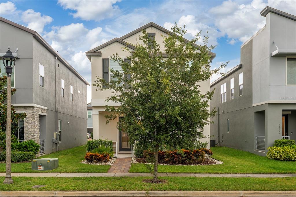A two-story house with a light-colored facade, a front tree, and a paved walkway — 10361 AUSTRINA OAK LOOP, WINTER GARDEN, FL
