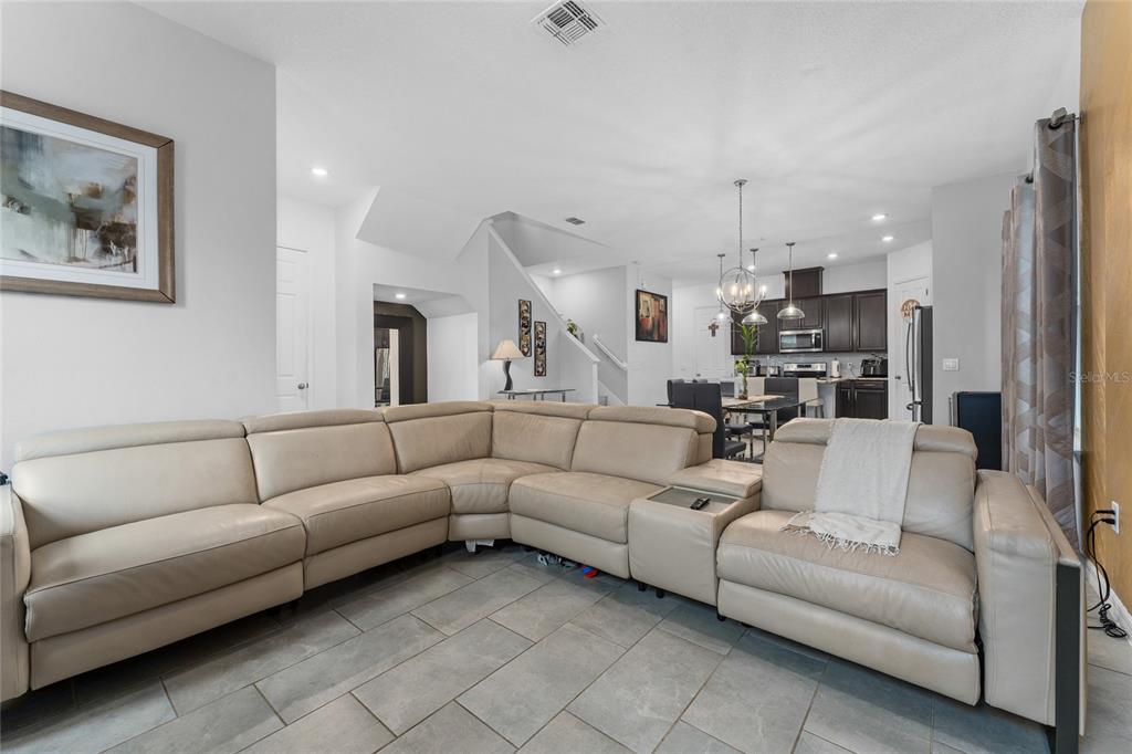 A spacious living room features a large beige sectional sofa on gray tile flooring — 10361 AUSTRINA OAK LOOP, WINTER GARDEN, FL