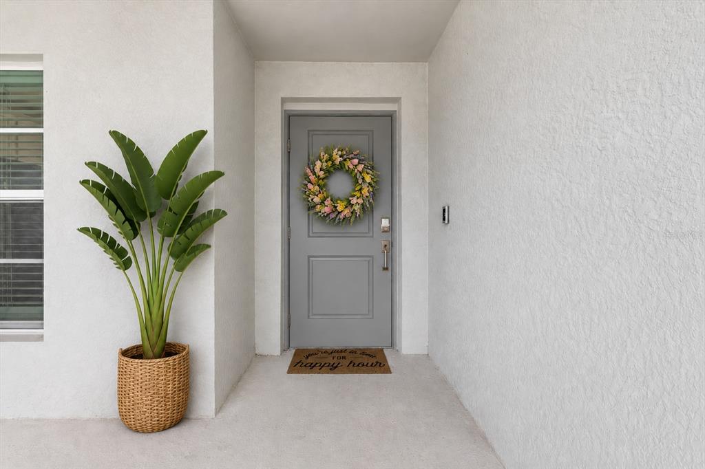 A gray front door with a floral wreath sits under a covered entryway — 12550 GALAPAGOS COURT UNIT 208, VENICE, FL