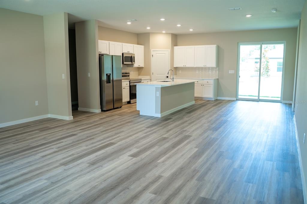 An open-concept kitchen and living area features wood-look flooring and a sliding glass door — 117 BAYSIDE DRIVE, PALM COAST, FL
