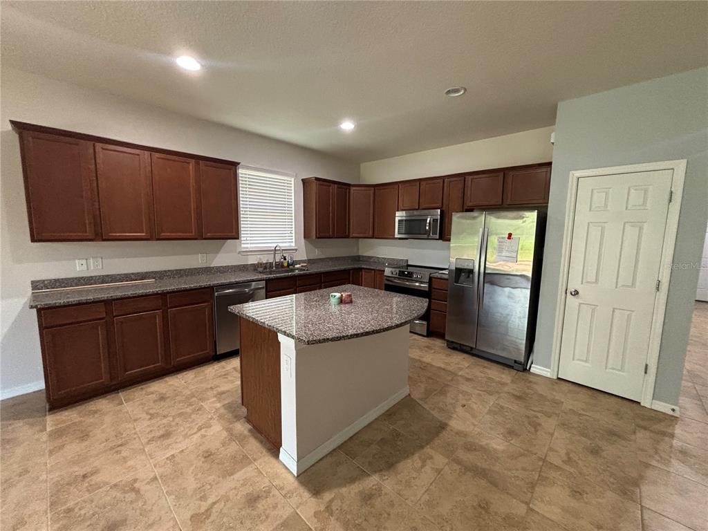 A kitchen features dark wood cabinets, granite countertops, a center island, and stainless steel appliances — 6122 100TH AVENUE E, PARRISH, FL