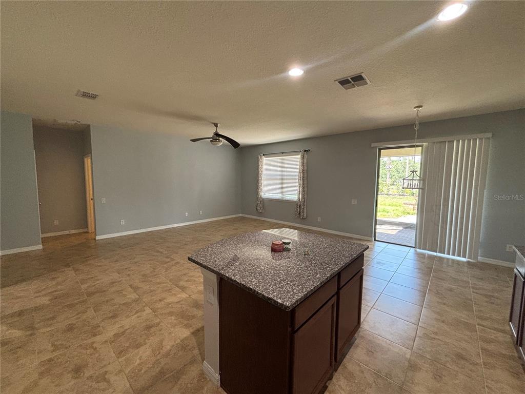 An open-concept kitchen and living area features tile flooring, a granite-topped island, and sliding doors — 6122 100TH AVENUE E, PARRISH, FL
