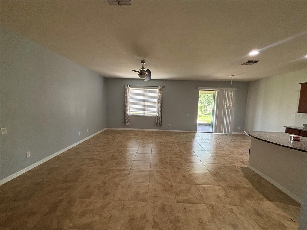 A spacious living area features light blue walls, tiled floors, a ceiling fan, and sliding doors — 6122 100TH AVENUE E, PARRISH, FL