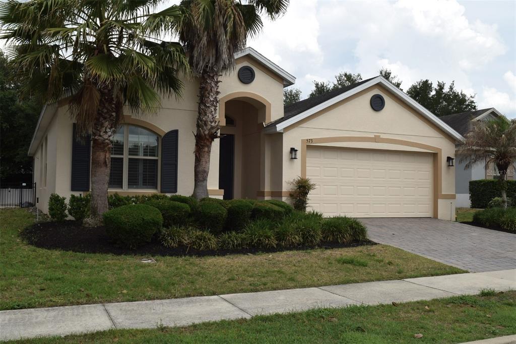 A single-story house with a beige stucco exterior, a two-car garage, and palm trees — 573 KISTLER CIRCLE, CLERMONT, FL