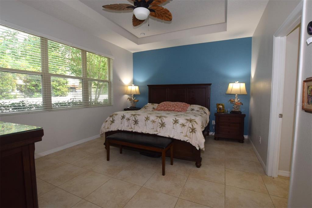 A bedroom features a blue accent wall, tile flooring, a ceiling fan, and large windows — 573 KISTLER CIRCLE, CLERMONT, FL