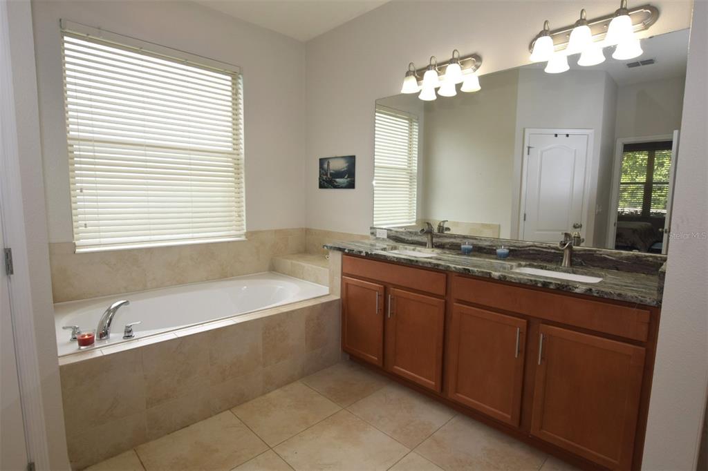 A bathroom features a soaking tub, a double-sink vanity with stone countertops, and tile flooring — 573 KISTLER CIRCLE, CLERMONT, FL