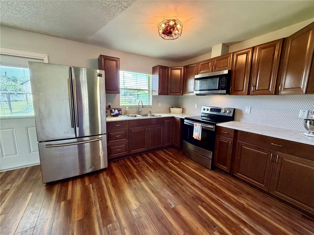 A kitchen features dark wood cabinets, stainless steel appliances, white countertops, and wood-look flooring — 8 N HENDRY AVENUE, FORT MEADE, FL