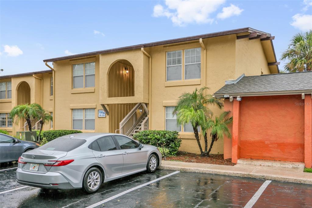 A two-story tan apartment building with a parking lot and a silver sedan in front — 758 E MICHIGAN STREET UNIT 210, ORLANDO, FL