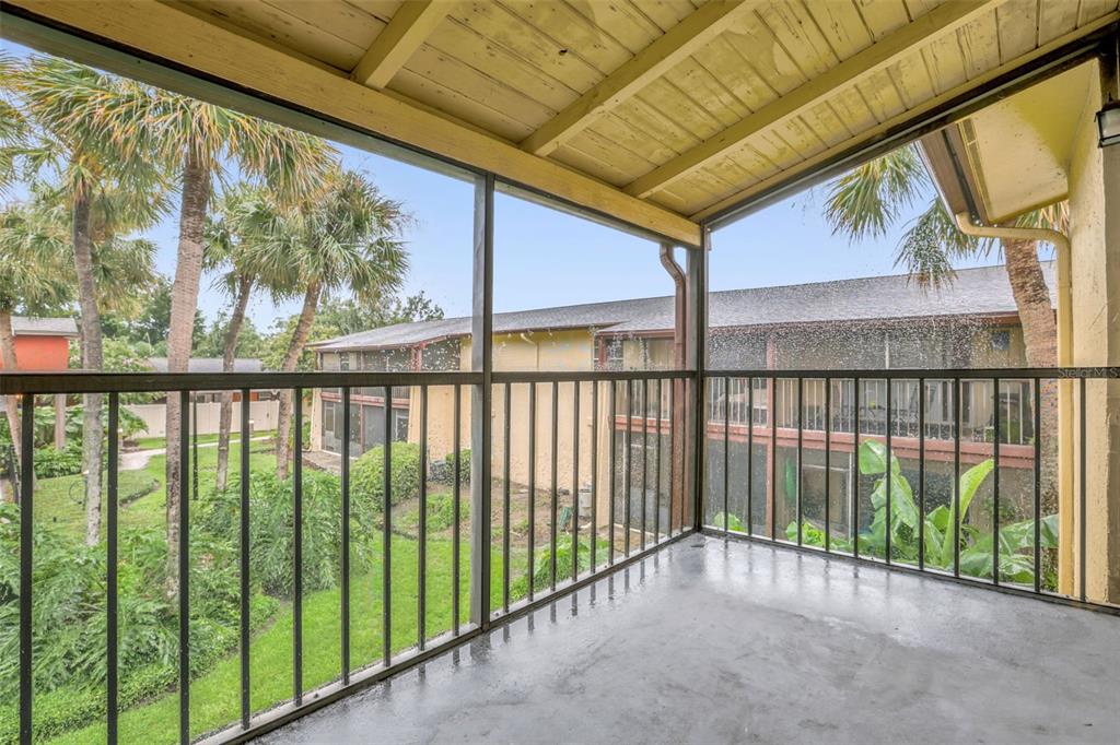 A covered, screened-in balcony with a concrete floor overlooks a grassy courtyard and palm trees — 758 E MICHIGAN STREET UNIT 210, ORLANDO, FL