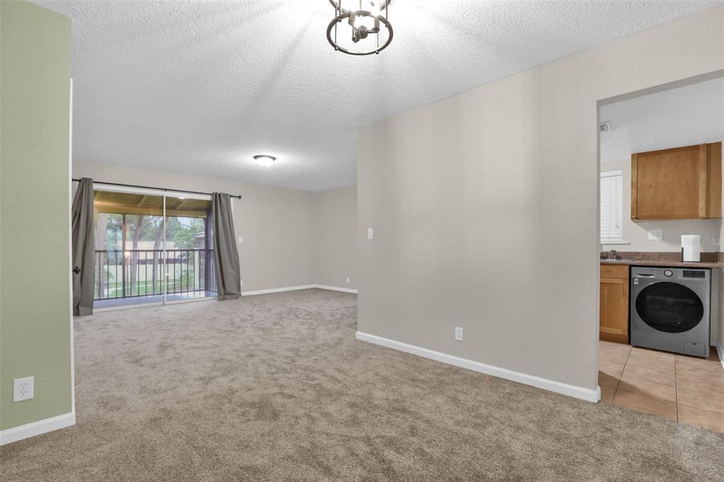 A carpeted living room with a sliding glass door leads to a balcony near a kitchen — 758 E MICHIGAN STREET UNIT 210, ORLANDO, FL